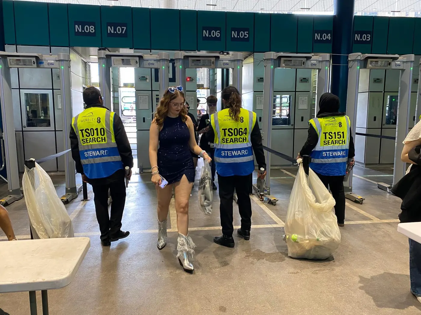 Stewards working search lanes beside walk-through metal detectors at a stadium entrance